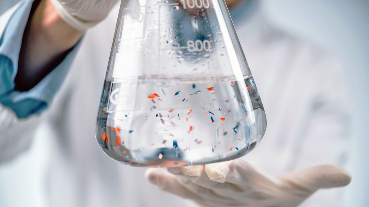 dil-ev-sicherheit-authentizitaet-chemische-analytik-Proben Nahaufnahme eines Laborkolbens mit klarer Flüssigkeit, in der farbige Partikel bzw. Probenbestandteile schweben. Eine Person mit Handschuhen hält den Kolben im Labor – Symbolbild für chemische Analytik, Qualitätskontrolle sowie Untersuchungen zur Lebensmittelsicherheit und Authentizität.