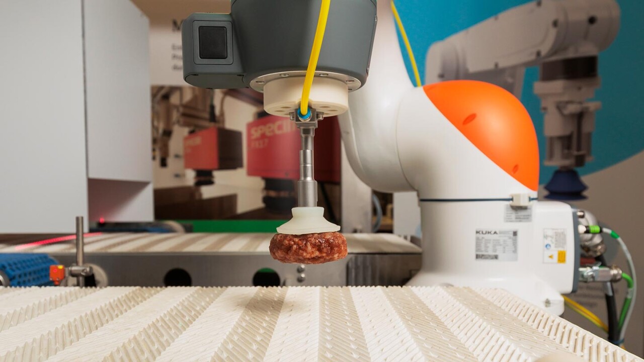 Nahaufnahme eines kollaborativen Roboters (Cobots) mit Vakuumgreifer, der ein geformtes Lebensmittelprodukt über einem Förderband anhebt und positioniert. Im Hintergrund ist weitere Automatisierungstechnik zu sehen. Das Bild steht für Robotik, automatisiertes Pick-and-Place, Prozessoptimierung, hygienisches Handling und Industrie-4.0-Anwendungen in der modernen Lebensmittelproduktion.