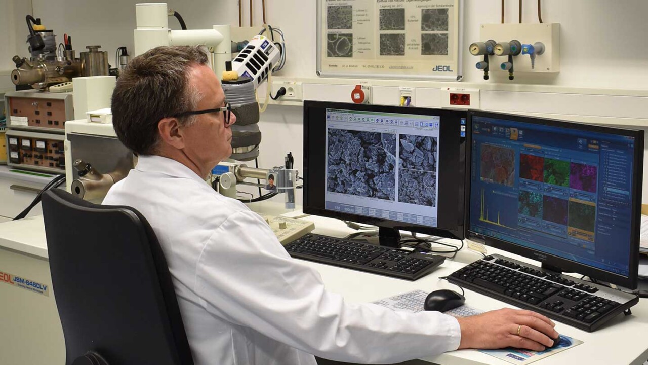 dil-ev-struktur-verarbeitung-struktur-und-funktionalitaet-Strukturanalyse-von-Proben-am-REM Ein Wissenschaftler im Laborkittel sitzt an einem Auswertungsplatz und analysiert Mikroskopieaufnahmen auf zwei Monitoren. Im Hintergrund ist ein Rasterelektronenmikroskop (REM) zu sehen; auf den Bildschirmen erscheinen hochauflösende Strukturbilder und Auswertedaten. Das Foto steht für Material- und Lebensmittelforschung, Strukturanalyse, Struktur-Funktionalität sowie die Untersuchung von Mikrostrukturen zur Bewertung von Verarbeitung, Qualität und Produkteigenschaften.