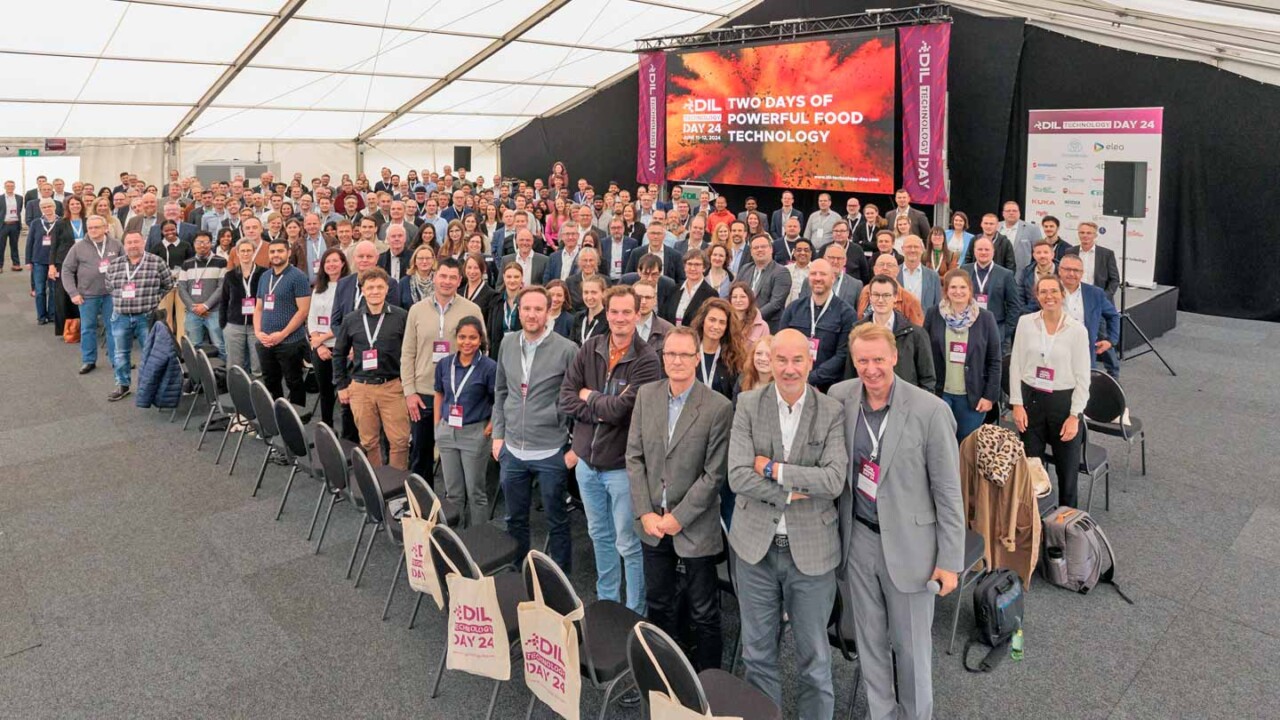 Großes Gruppenfoto beim DIL Technology Day 2024: Zahlreiche Teilnehmende stehen im Konferenzzelt vor der Bühne mit LED-Screen „Two Days of Powerful Food Technology“. Im Vordergrund sind Reihen von Stühlen und DIL-Taschen zu sehen. Das Bild zeigt die Community aus Wissenschaft, Industrie und Praxis sowie den Netzwerk-Charakter der Veranstaltung rund um Food Technology, Innovation und Kooperation.