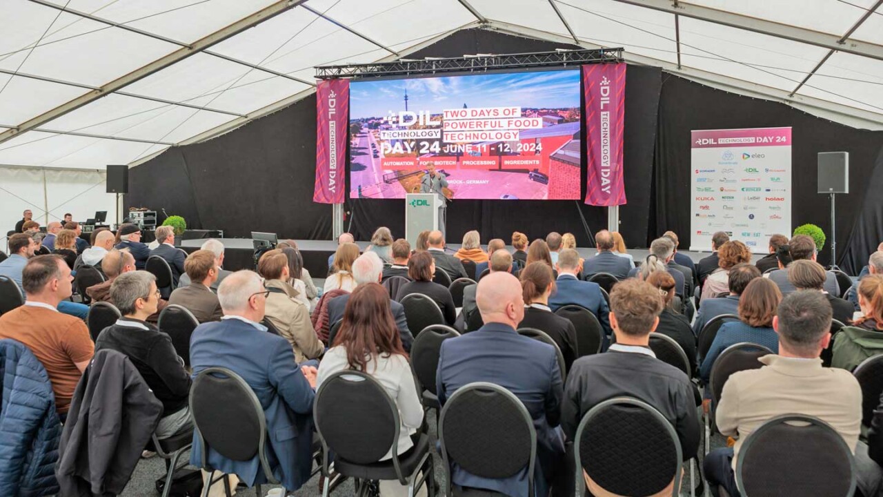 Großes Publikum sitzt in einem Konferenzzelt und verfolgt einen Vortrag auf der Bühne. Auf der LED-Wand ist „DIL Technology Day 24“ zu sehen, daneben eine Sponsoren- bzw. Partnerwand. Das Foto zeigt die Atmosphäre einer Fachveranstaltung mit Vorträgen, Networking und aktuellen Themen rund um Lebensmitteltechnologie, Automatisierung, Processing und Ingredients.