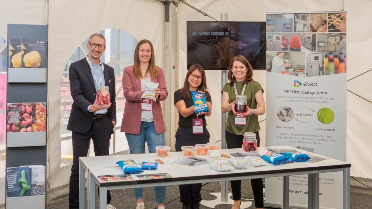 Vier Personen stehen an einem Messe-/Eventstand und präsentieren Lebensmittelproben in Gläsern sowie Snackprodukte. Vor ihnen befindet sich ein Tisch mit Produktmustern und Verpackungen. Im Hintergrund sind ein Monitor und ein Roll-up zu „PEFPilot Dual systems“ (elea) sowie weitere Infotafeln zu sehen.