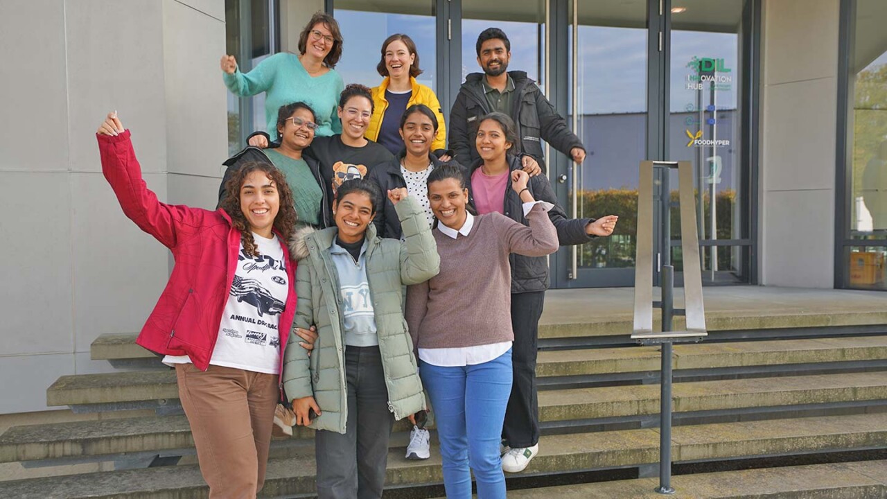 Gruppenfoto vor dem Gebäude: Studierende und Mitarbeitende stehen gemeinsam auf einer Treppe, lächeln und zeigen Teamgeist. Im Hintergrund ist der Eingang mit DIL-Branding zu sehen. Das Bild steht für den Masterstudiengang „Food Process and Product Engineering (FPPE)“, internationale Zusammenarbeit, praxisnahe Weiterbildung und Vernetzung am DIL.