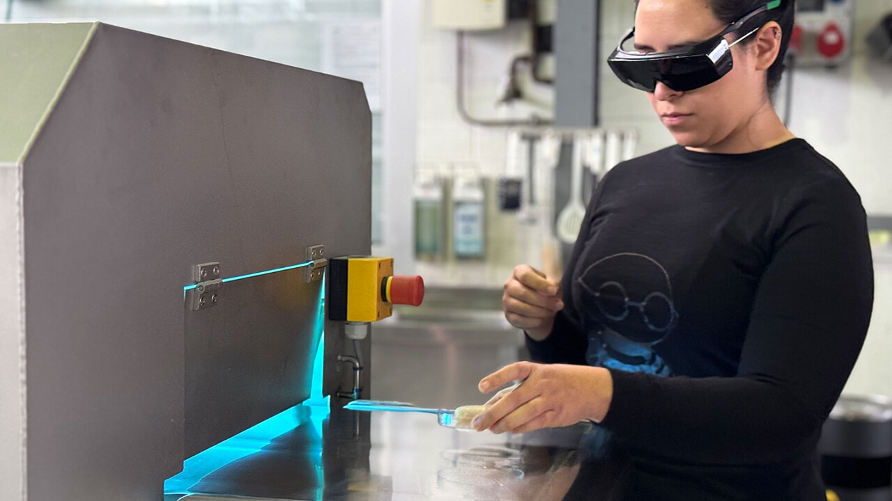 Eine Person trägt Schutzbrille und arbeitet an einer Laborstation mit blauem Licht/UV-Beleuchtung. Mit einer Probe in einer Petrischale bzw. auf einem Träger wird eine optische Prüfung oder Detektion durchgeführt. Das Bild steht für praxisnahe Laborlehre, moderne Analytik, Qualitätskontrolle und experimentelles Arbeiten im Masterstudiengang „Food Process and Product Engineering (FPPE)“ – mit Fokus auf Mess- und Prüftechnik in der Lebensmittelwissenschaft.